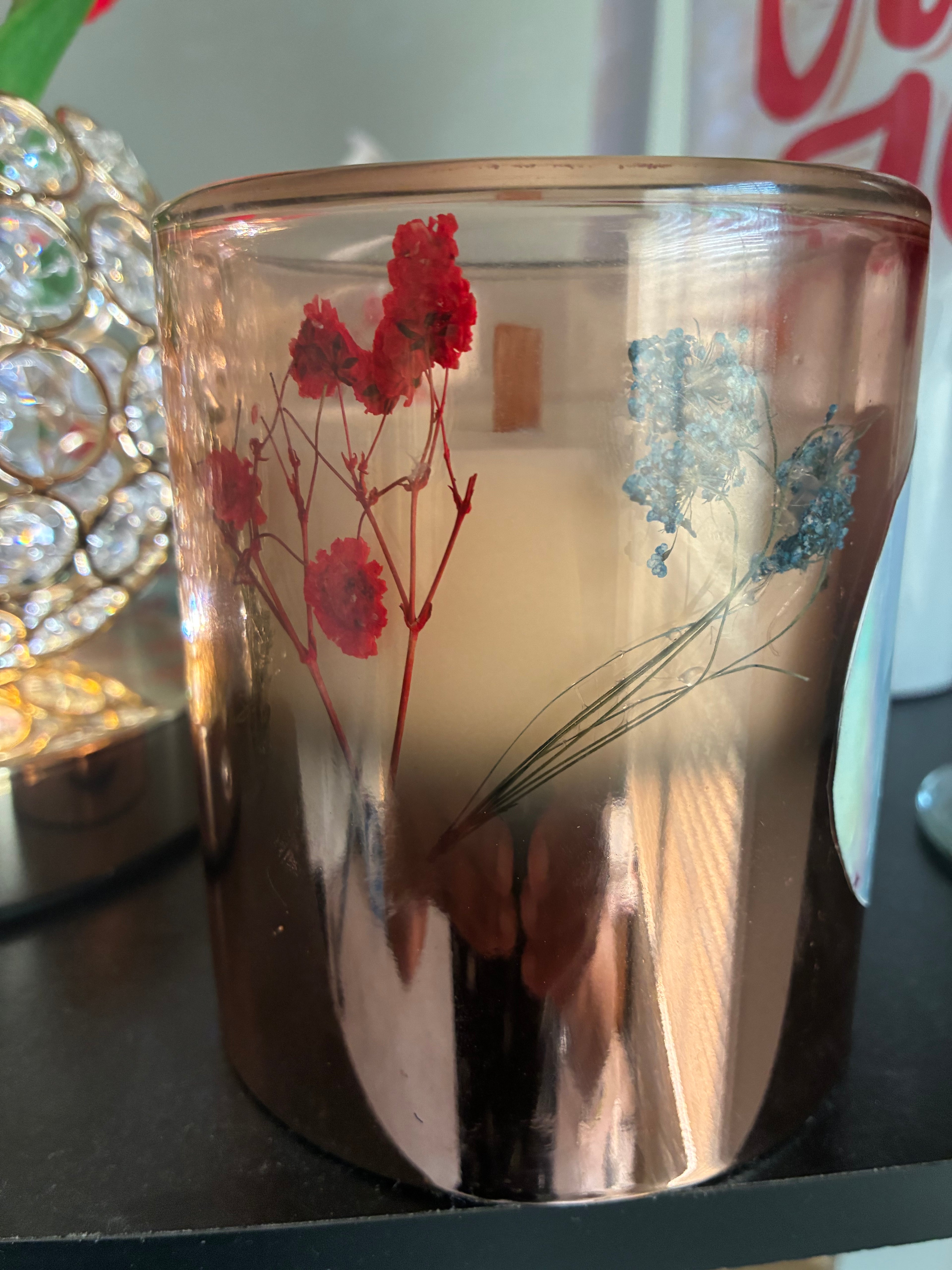 Pressed botanical candle with red and blue dried flowers in amber glass